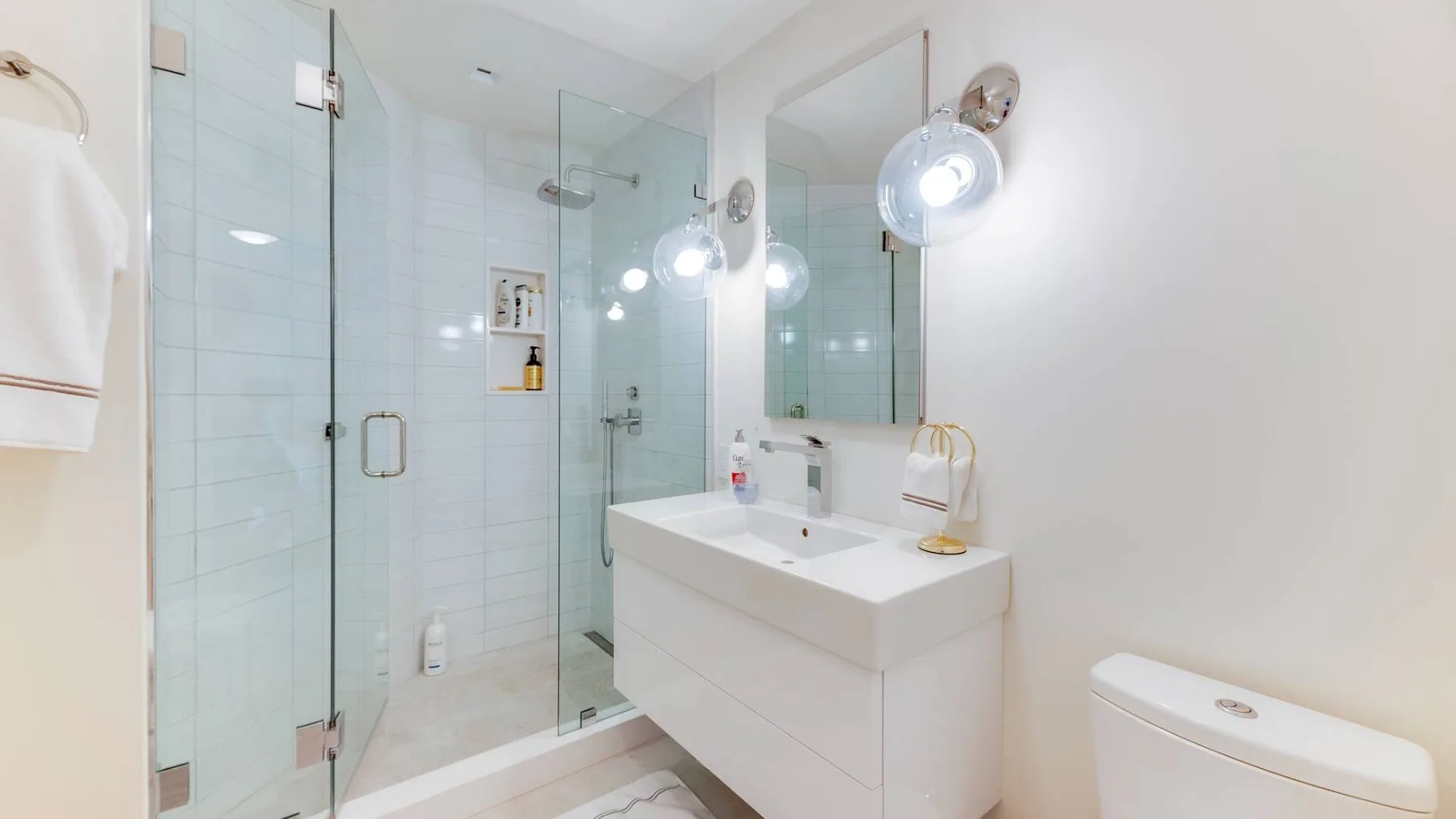 Un baño luminoso con una ducha de vidrio y un lavabo blanco.
