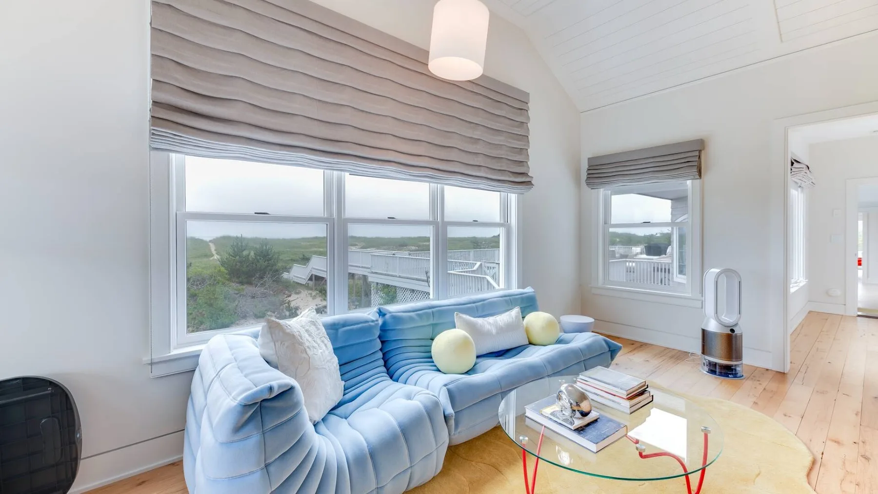 Una sala luminosa con asientos azules, grandes ventanas y una mesa de centro de vidrio.