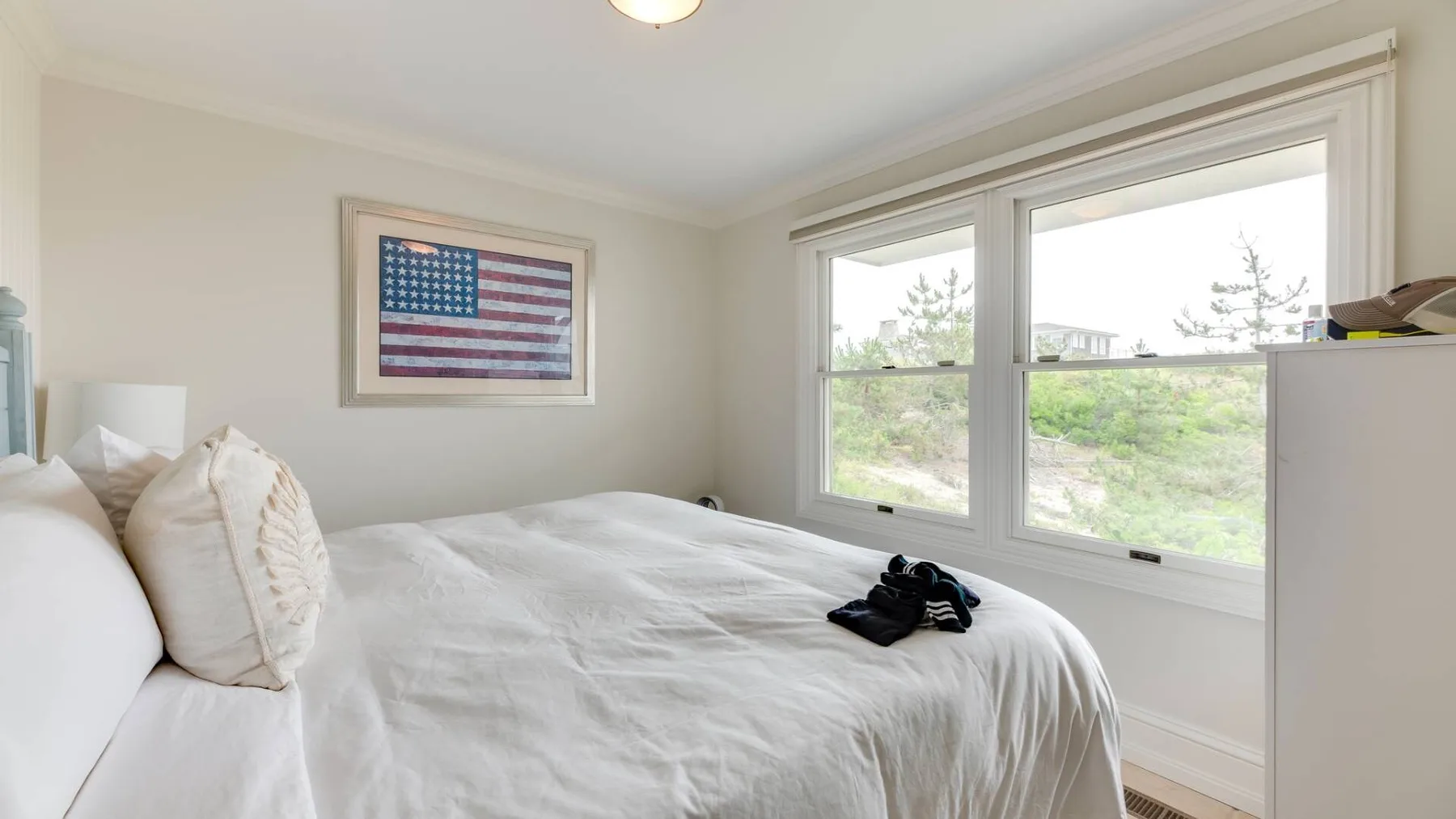 Un dormitorio con una cama blanca junto a grandes ventanas.