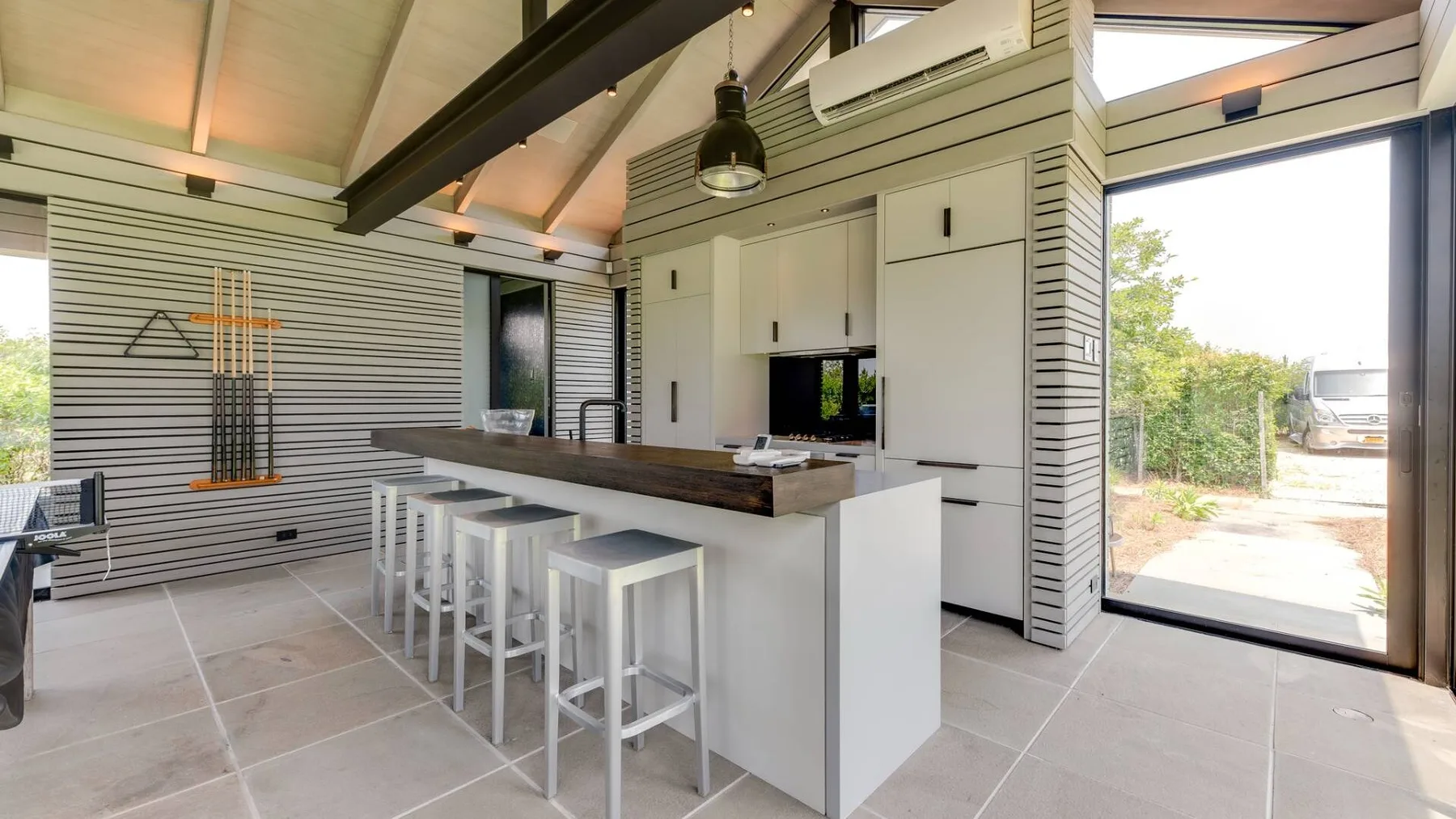 Una cocina moderna y luminosa con una isla larga y taburetes junto a grandes ventanales.