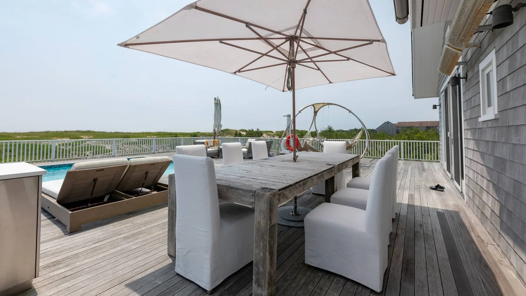 Una zona de comedor al aire libre junto a una piscina, con mesa y sombrilla.