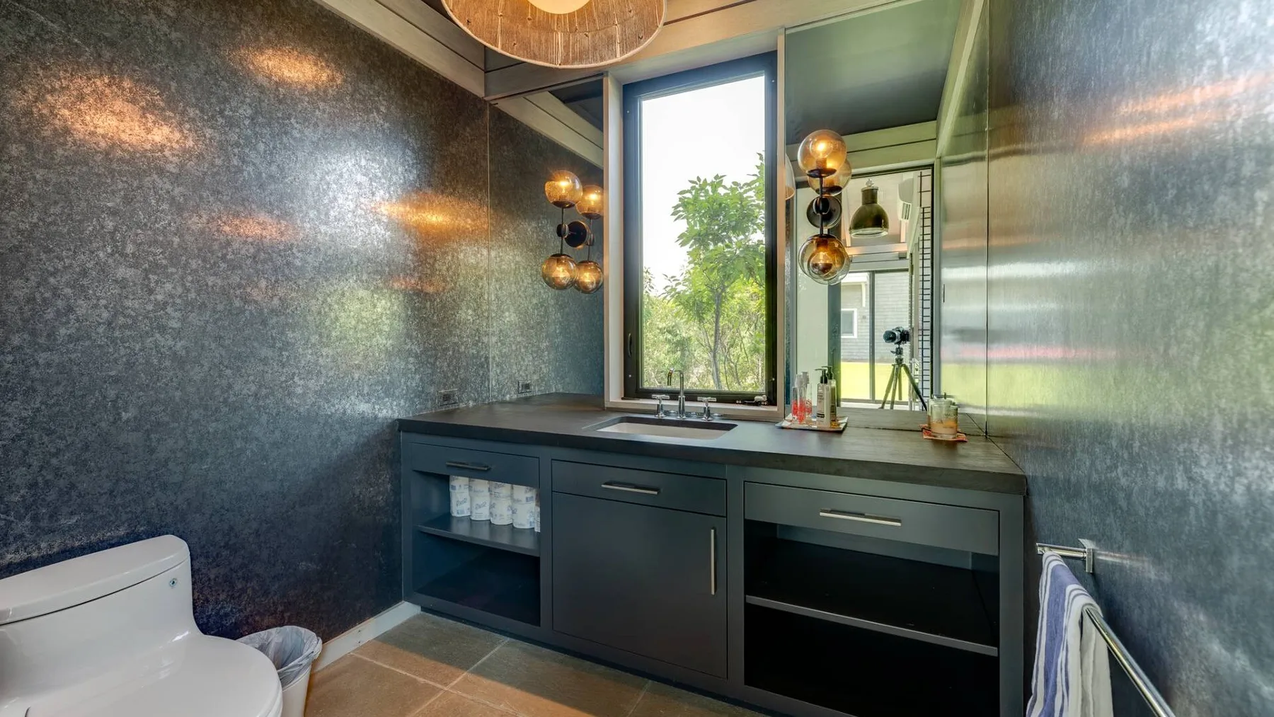 Un baño moderno con un tocador oscuro, un espejo grande y una ventana.
