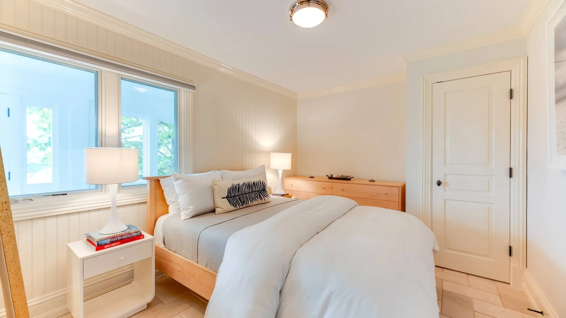Un dormitorio luminoso con una cama bien tendida junto a grandes ventanas.