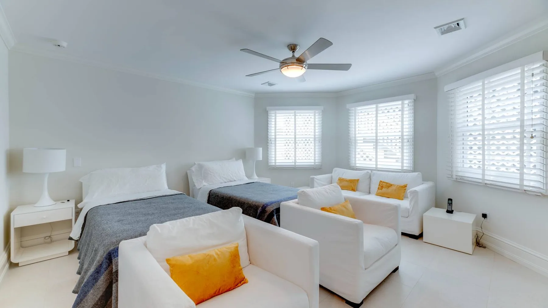 Un dormitorio luminoso con zona de estar, camas, sillones y grandes ventanas.