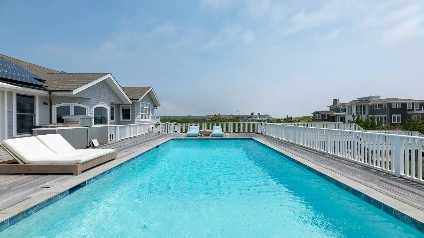 Piscina al aire libre junto a una casa, con asientos de descanso en la terraza.