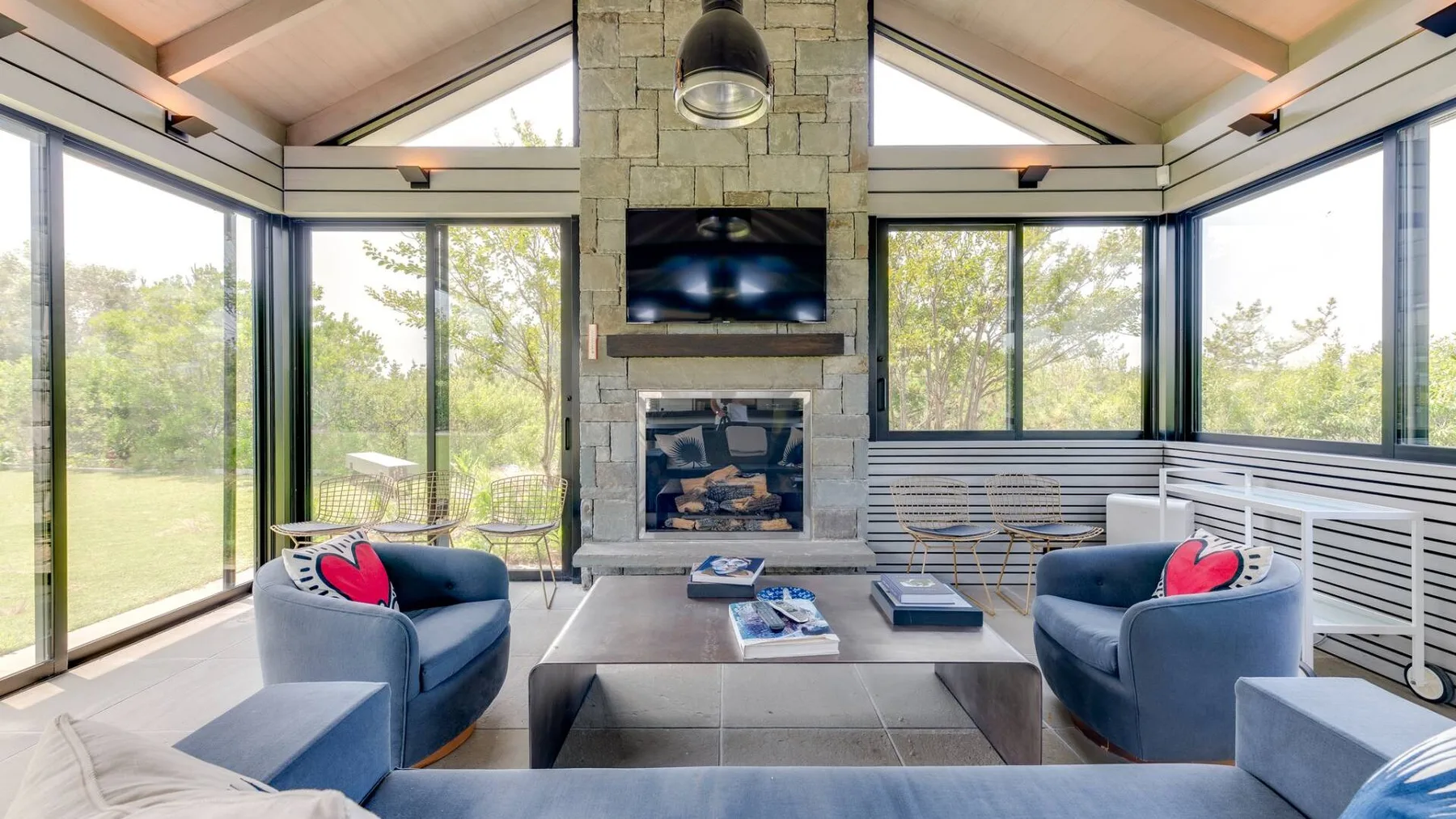 Una sala luminosa tiene grandes ventanales, asientos y una chimenea de piedra.