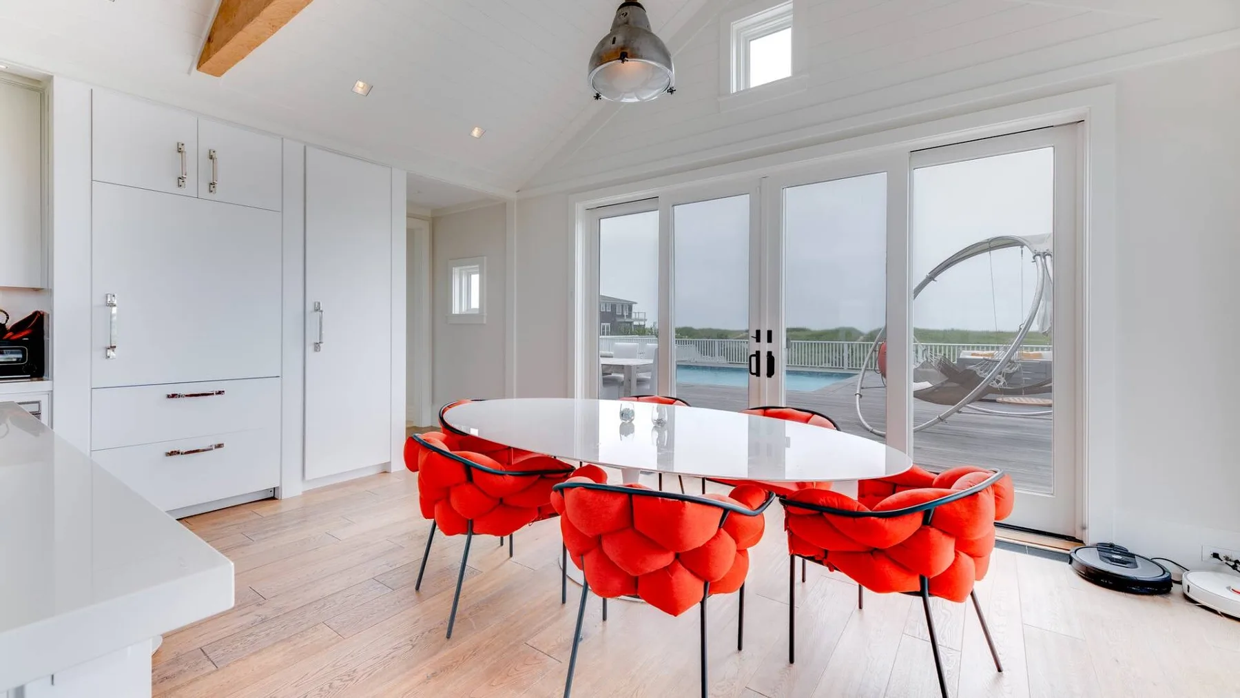 Un comedor luminoso con una mesa larga y asientos rojos junto a puertas de vidrio.