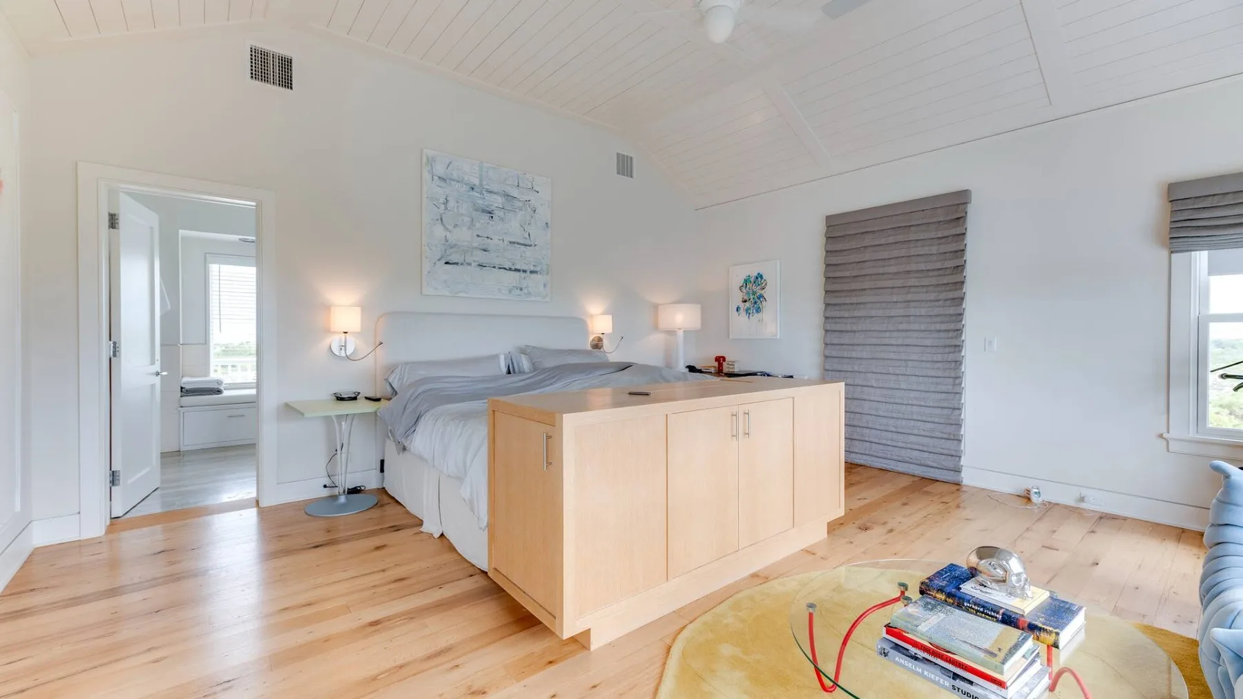 Un dormitorio luminoso con una cama, suelo de madera clara y techo alto inclinado.