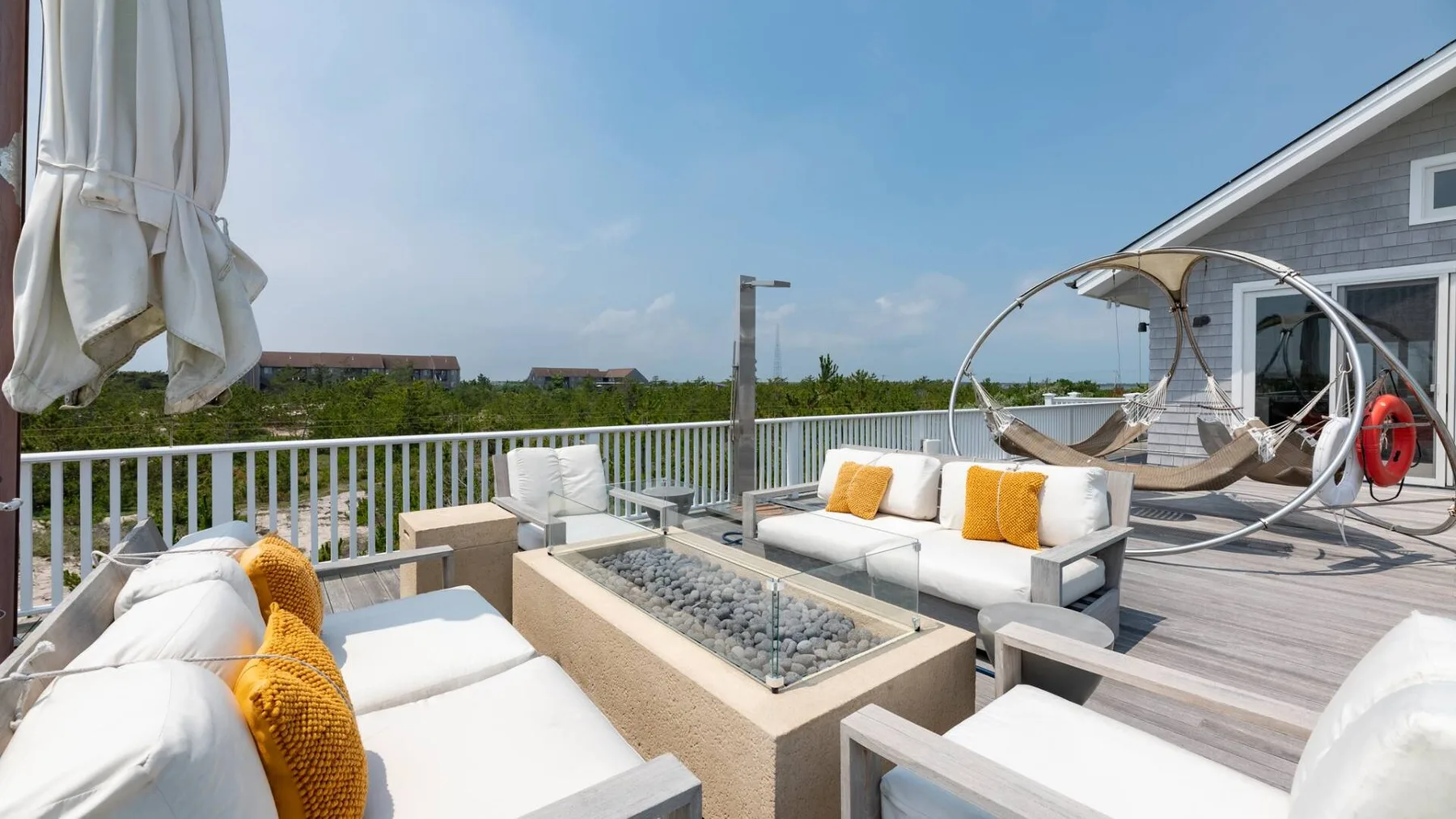 Un patio al aire libre con asientos acolchados, una hoguera rectangular y una silla colgante.