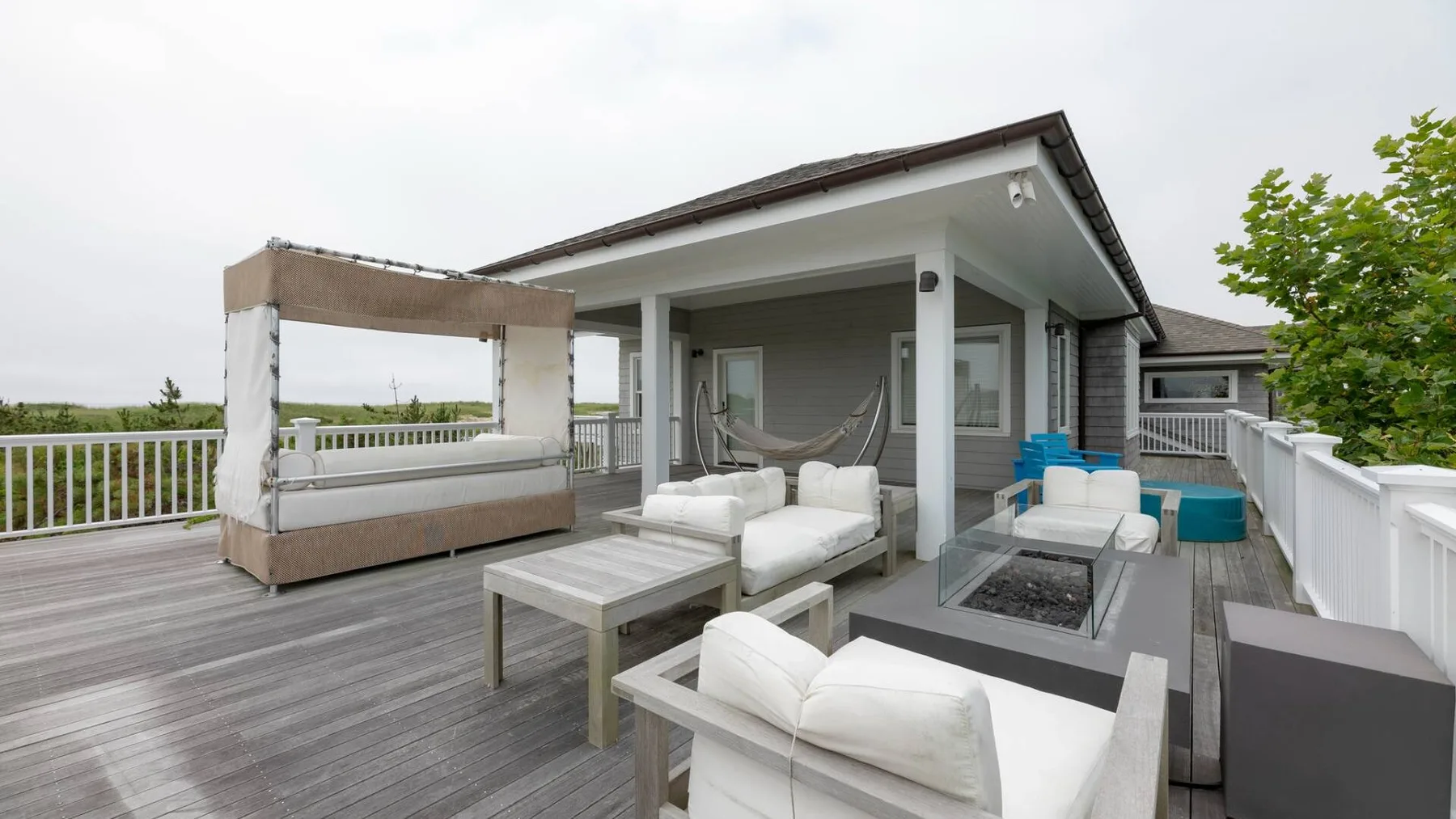 Una terraza exterior tiene asientos alrededor de una mesa baja junto a una casa moderna.