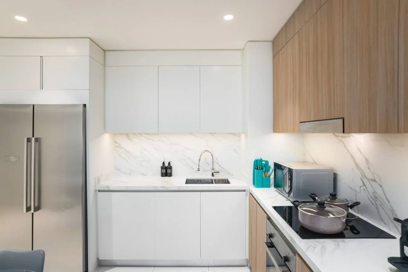 Una cocina moderna y luminosa con gabinetes blancos, refrigerador y electrodomésticos.