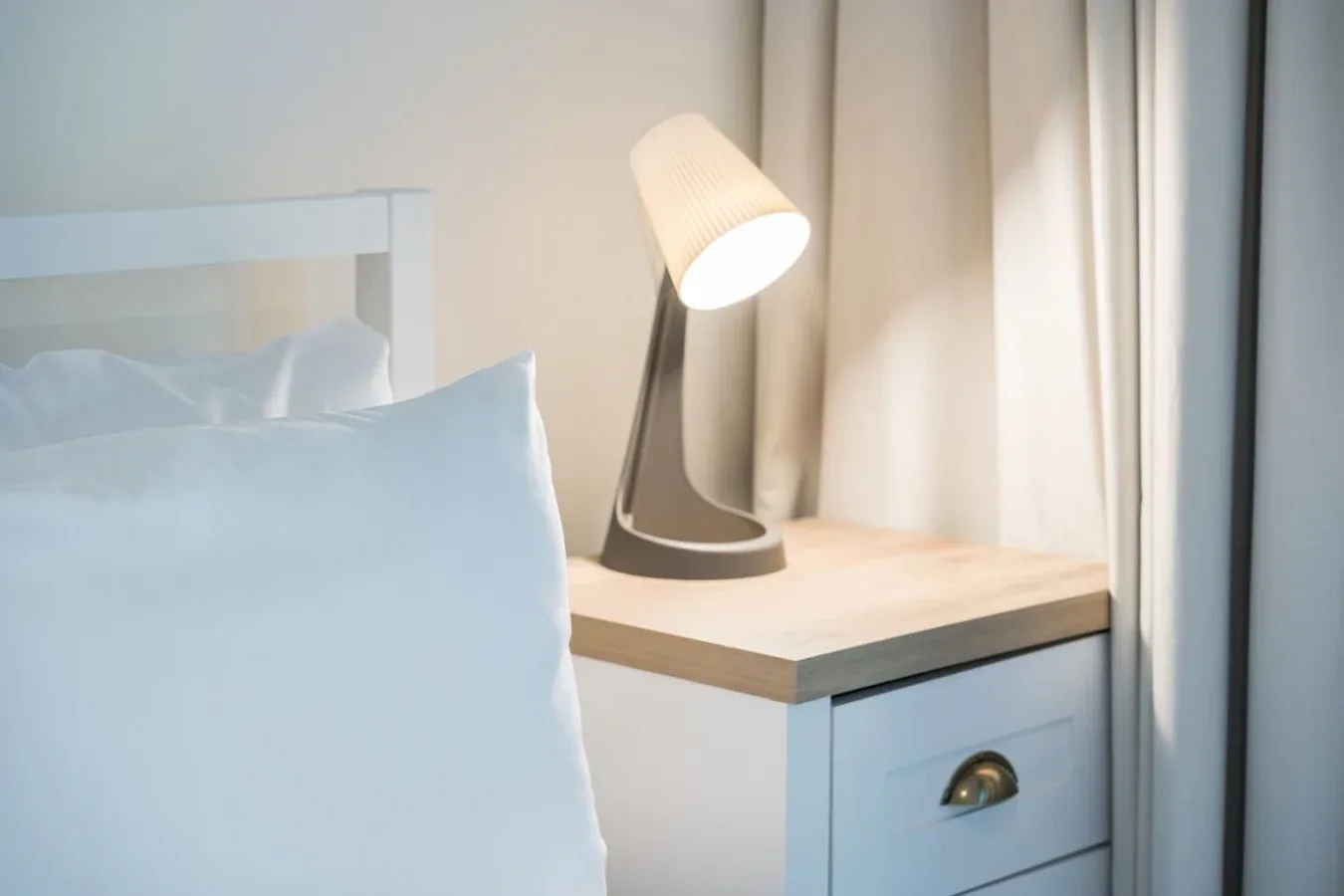 Rincón de dormitorio con una mesita de noche y una lámpara encendida junto a la cama.