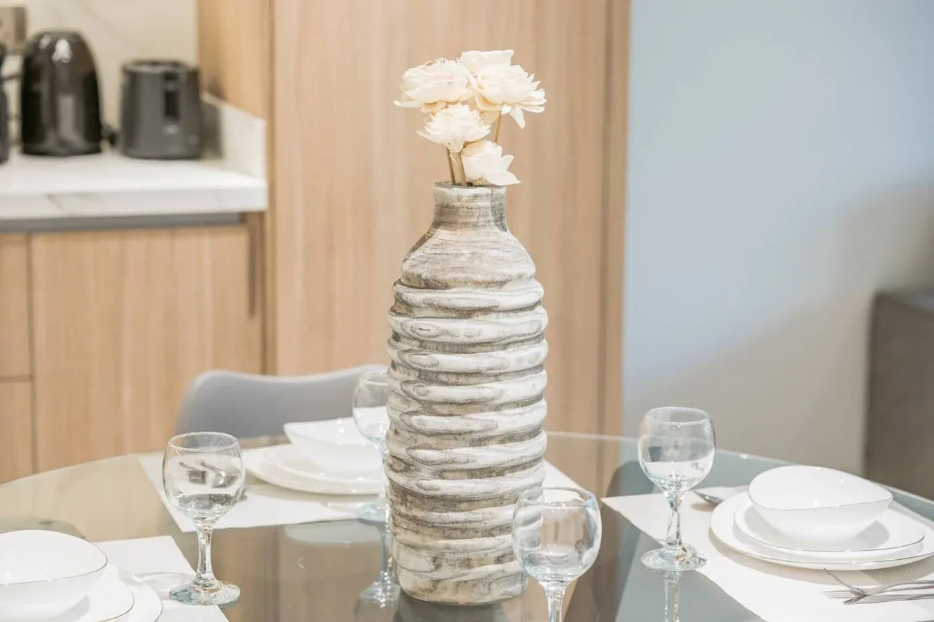 Una mesa de comedor está puesta con platos y copas, con un jarrón de flores en el centro.