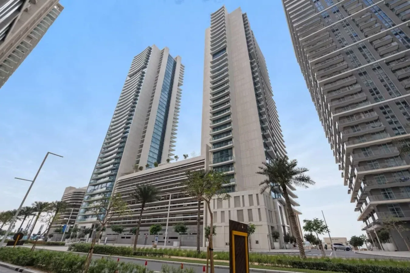 Altas torres residenciales se elevan sobre una calle ajardinada con palmeras.