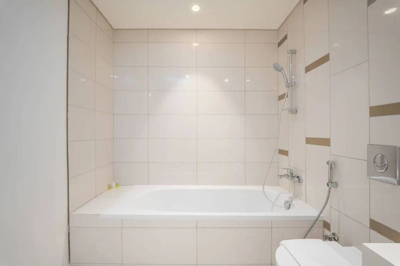 Un baño alicatado con bañera, grifería de ducha y parte de un inodoro.