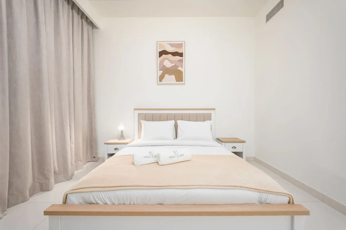 Un dormitorio luminoso con una cama tendida y cortinas junto a la ventana.