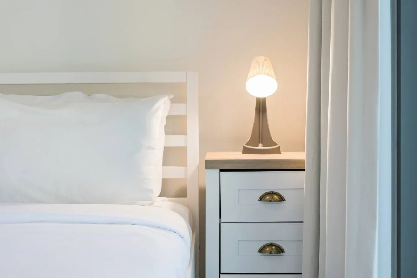 Un dormitorio con una cama tendida junto a una lámpara encendida.