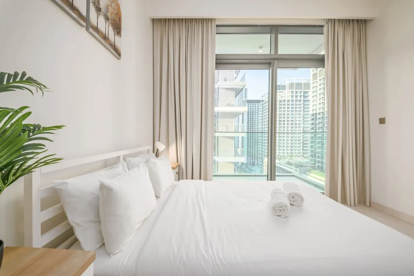Un dormitorio luminoso con una cama blanca frente a una ventana grande y un balcón.