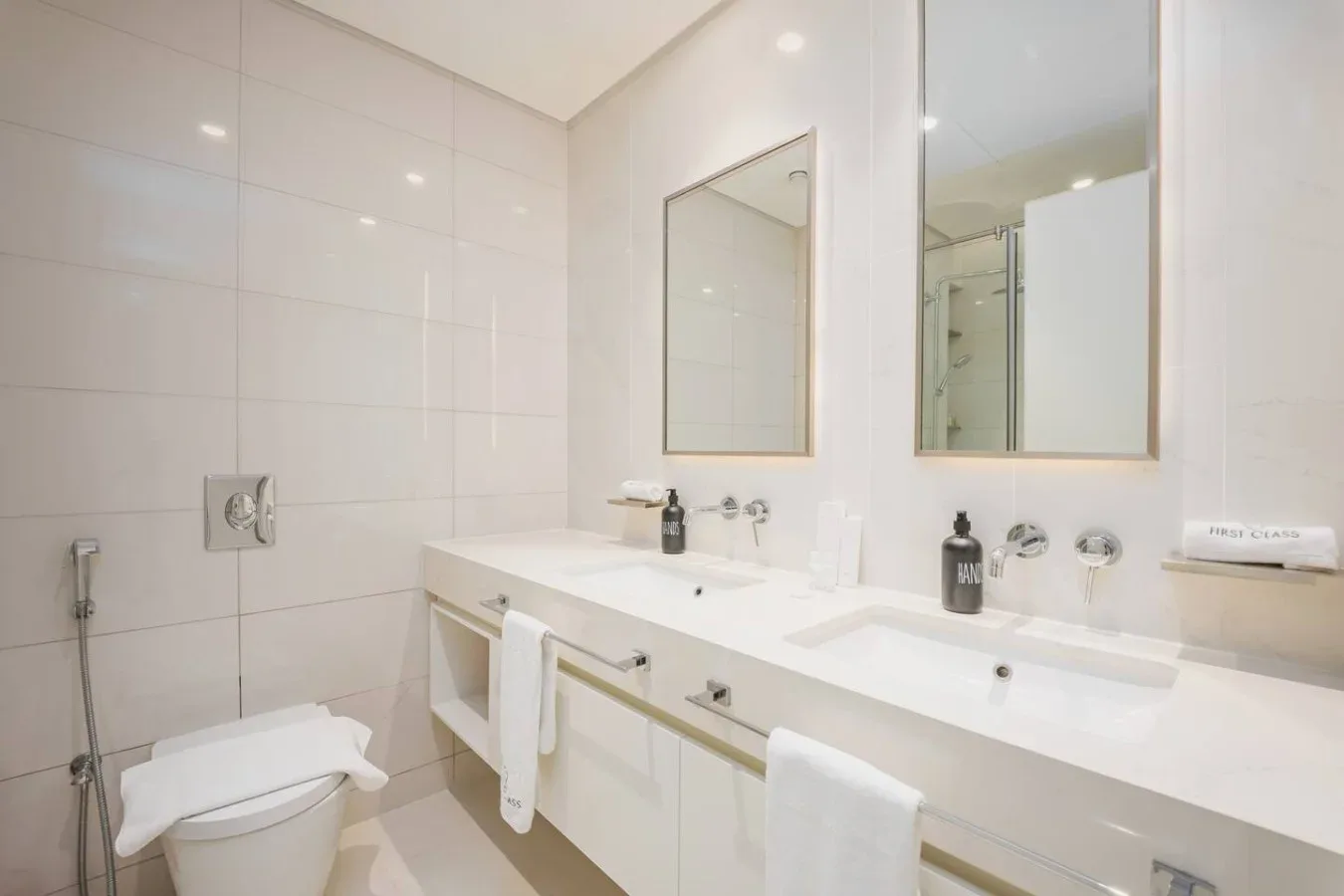 Un baño luminoso con azulejos, un mueble de lavabo largo y un inodoro.