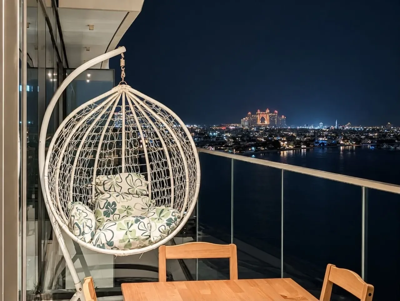 Una zona de estar en un balcón tiene vistas al horizonte de la ciudad por la noche.
