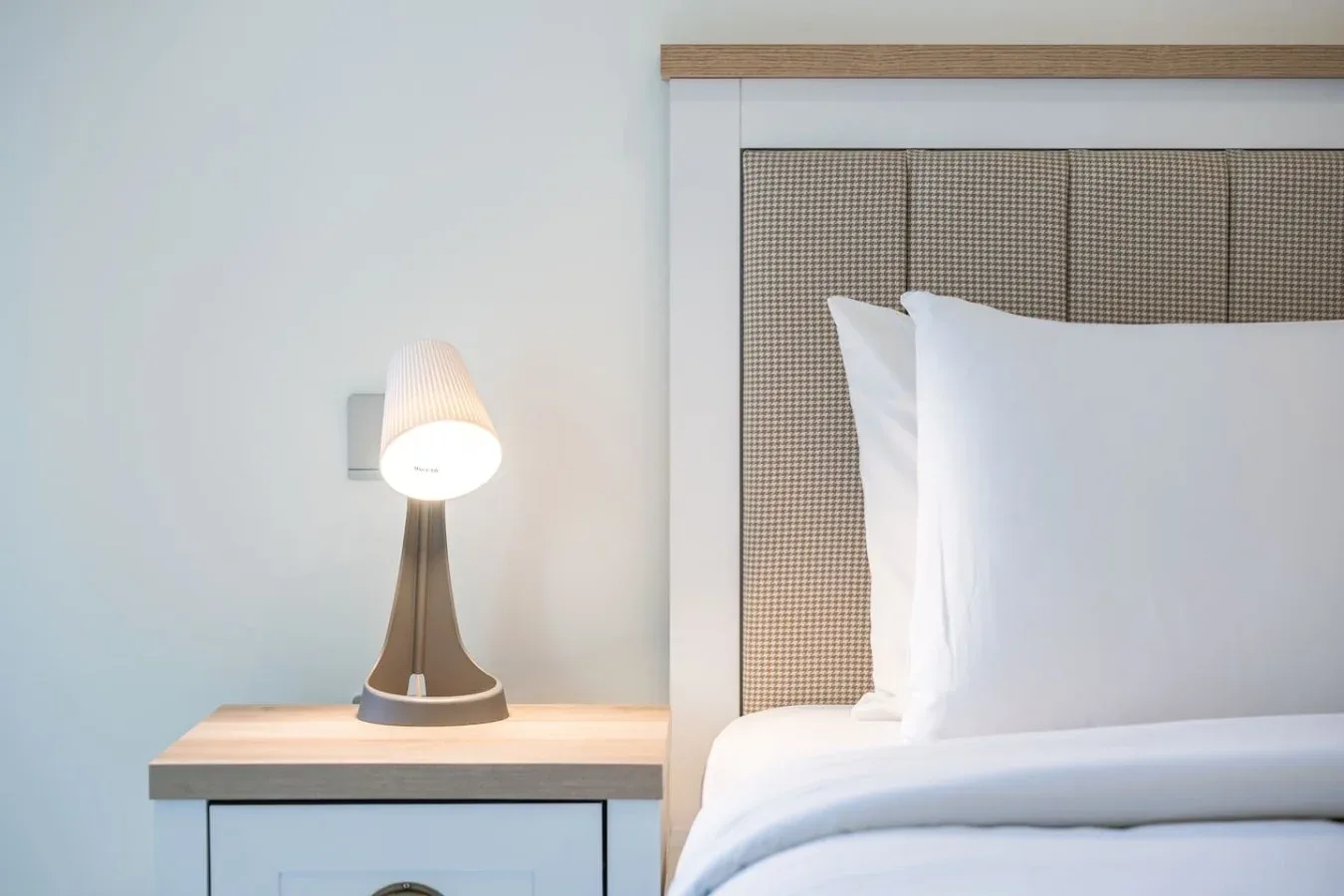 Dormitorio con una cama bien arreglada junto a una lámpara encendida.
