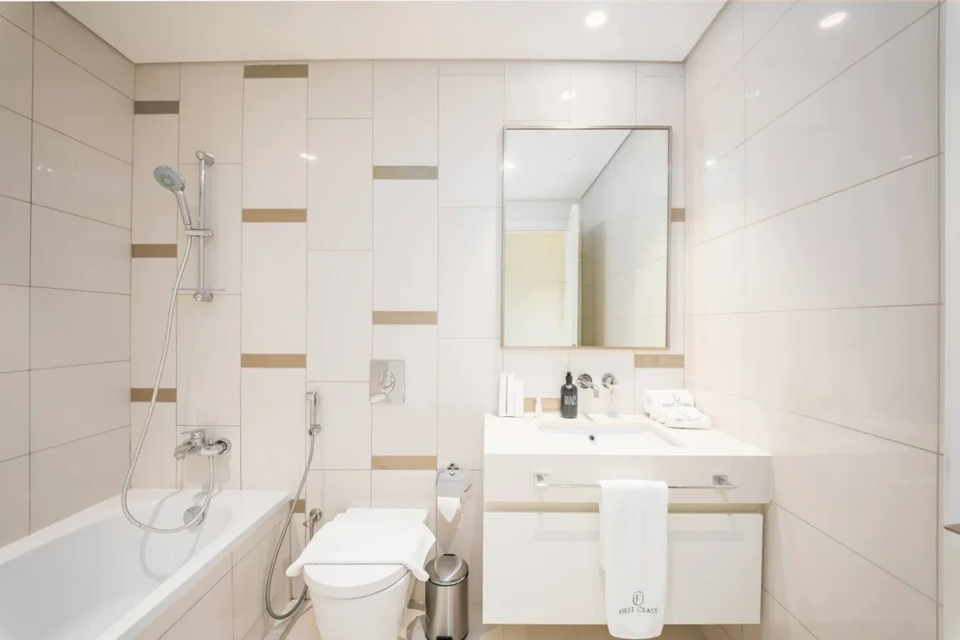 Un baño luminoso con bañera, ducha y tocador bajo un espejo.