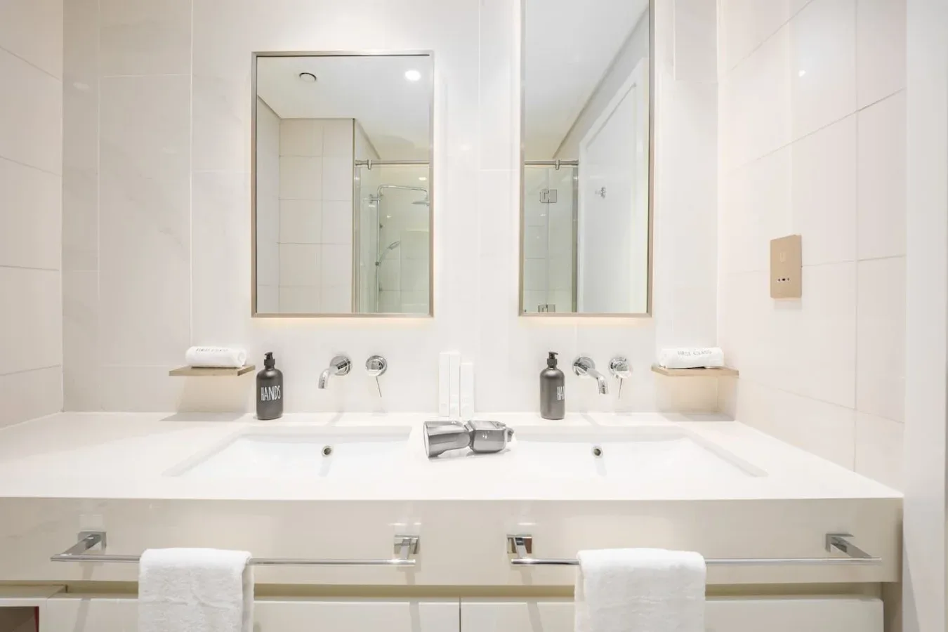 Un baño luminoso con azulejos, una encimera larga con lavabos y espejos.