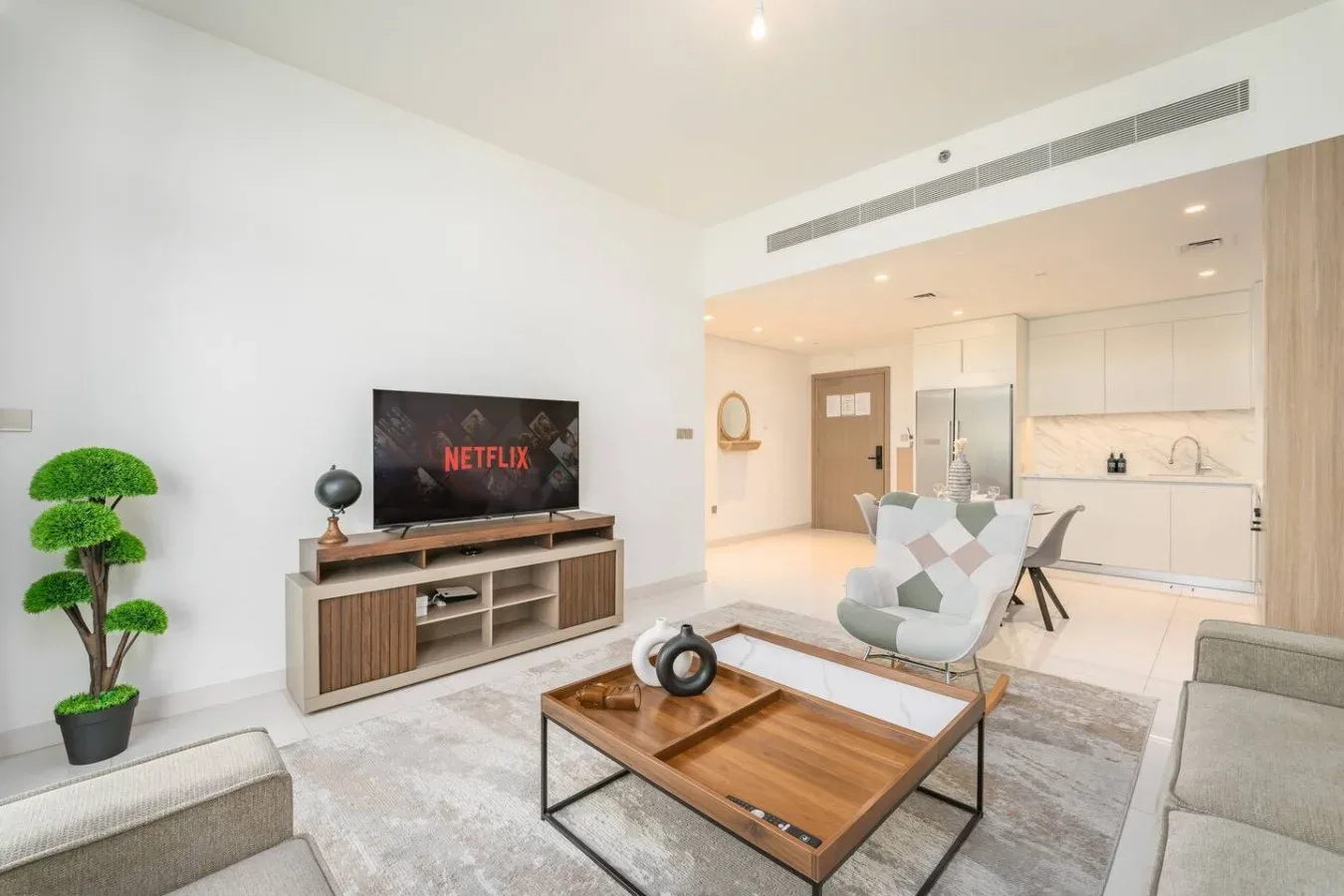 Una luminosa sala de estar abierta con televisión, asientos y una cocina contigua.
