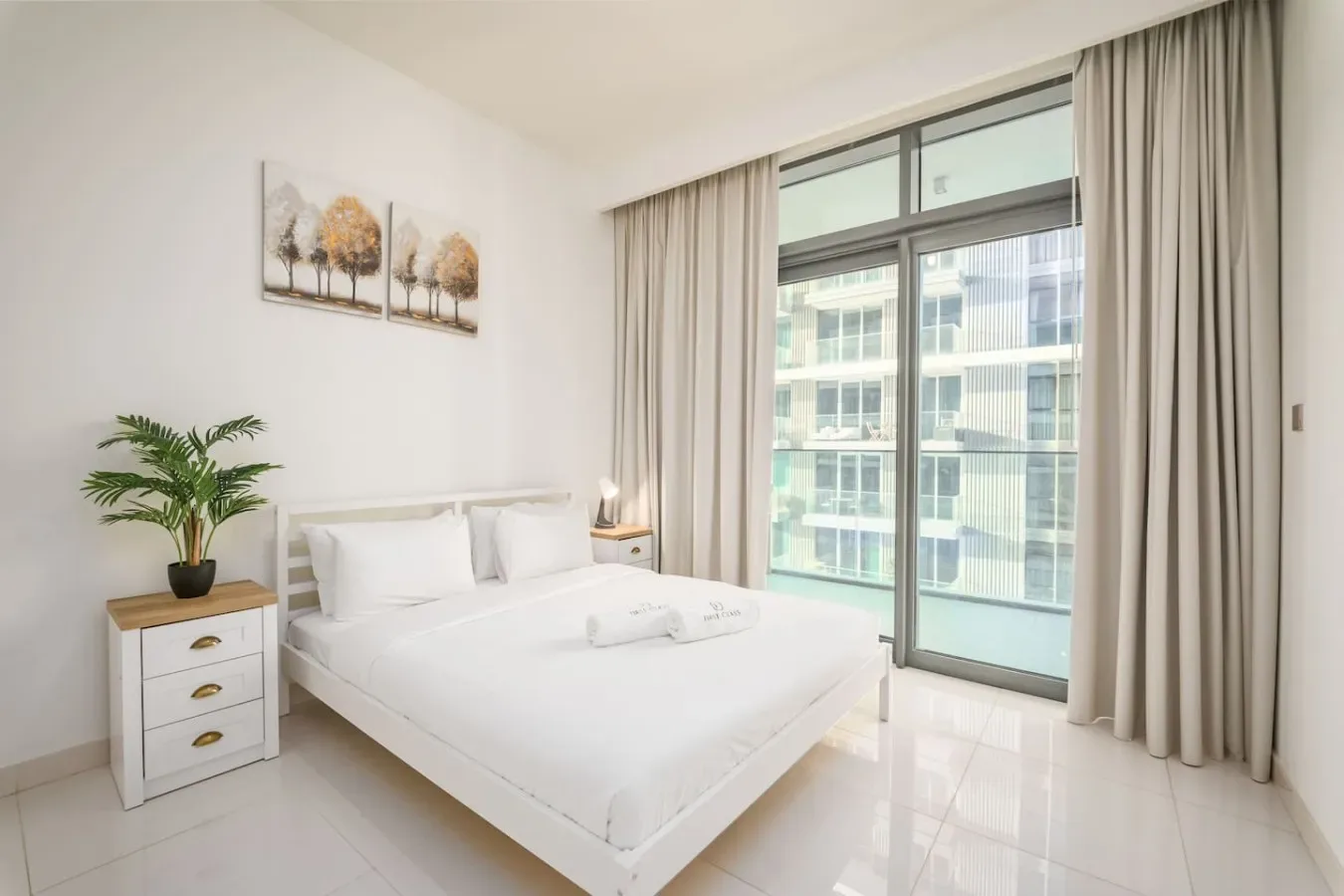 Un dormitorio luminoso con una cama bien hecha junto a una gran ventana con cortinas.