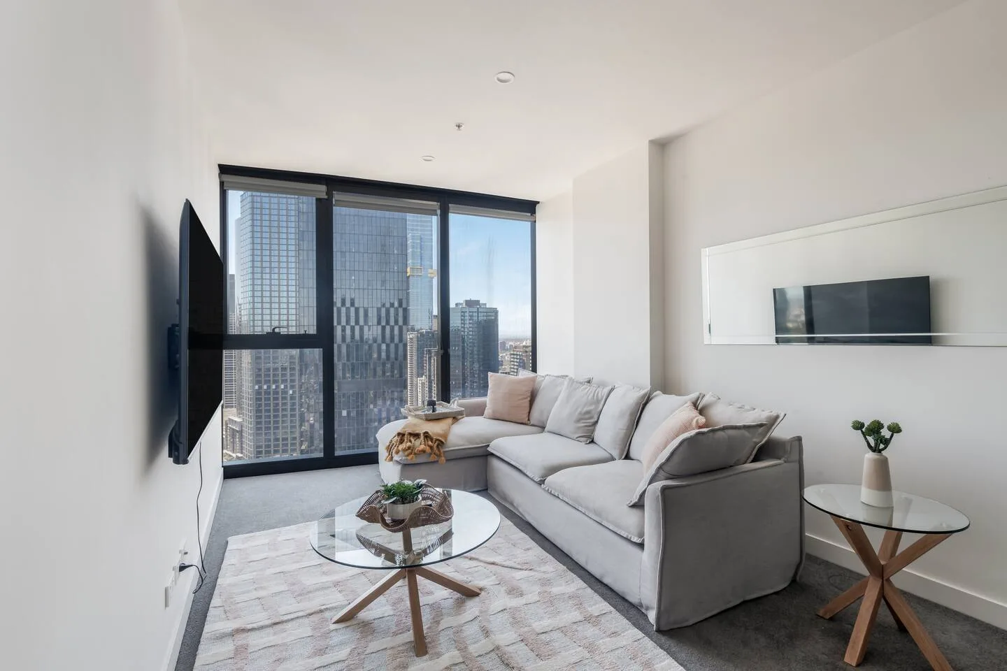 Una sala de estar con asientos, una mesa de centro redonda y grandes ventanas con vistas a edificios de la ciudad.