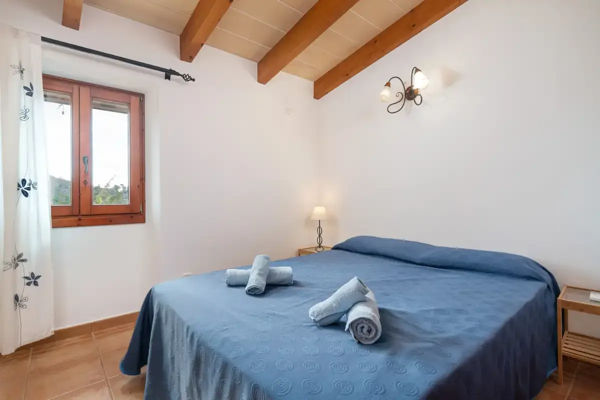 A bedroom with a blue-covered bed beneath exposed wooden ceiling beams.