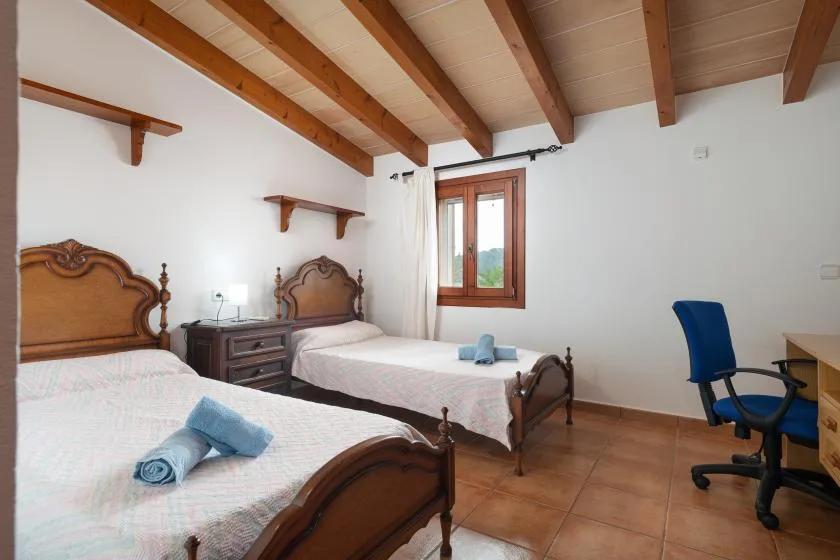 A bedroom with two beds and a desk beneath exposed ceiling beams.