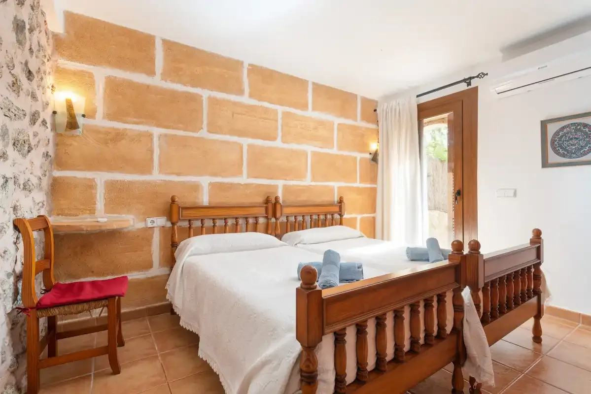 A bedroom with two wooden beds, white bedding, and a brick-patterned wall.