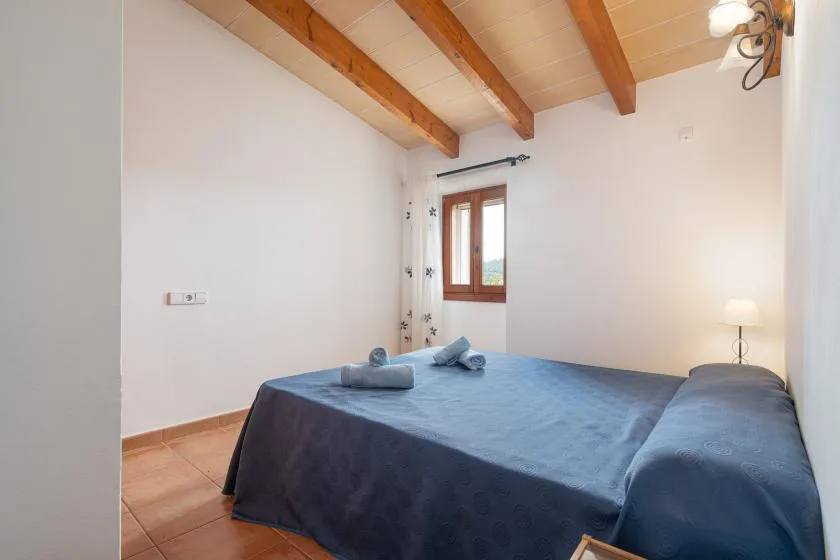 A bedroom with a bed covered in blue bedding beneath exposed wooden ceiling beams.