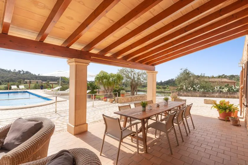 A covered outdoor patio with a dining table and a swimming pool nearby.