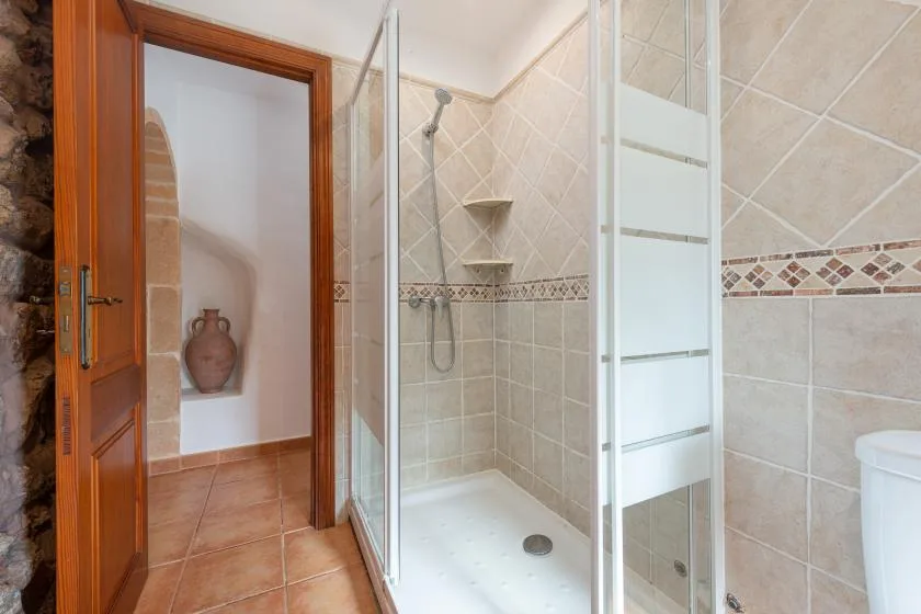 A tiled bathroom with a glass shower and an open wooden door.
