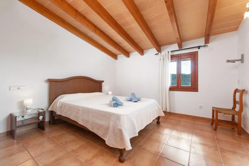 A bedroom with a double bed, exposed wooden ceiling beams, and a window.
