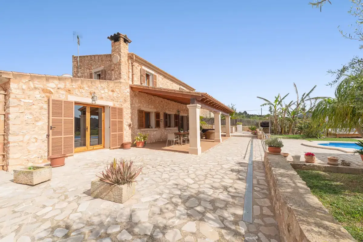 A stone house opens onto a paved patio beside a swimming pool.