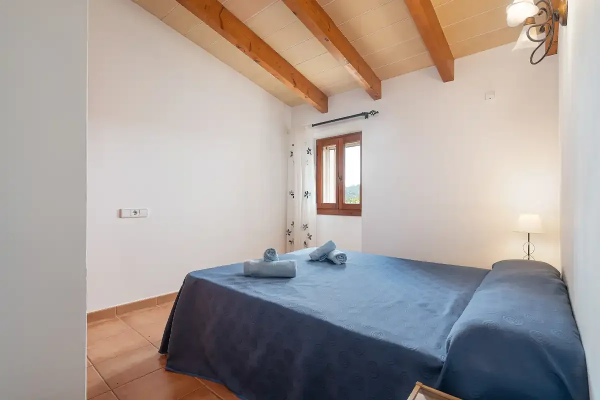 A bedroom with a bed covered in blue bedding beneath exposed wooden ceiling beams.