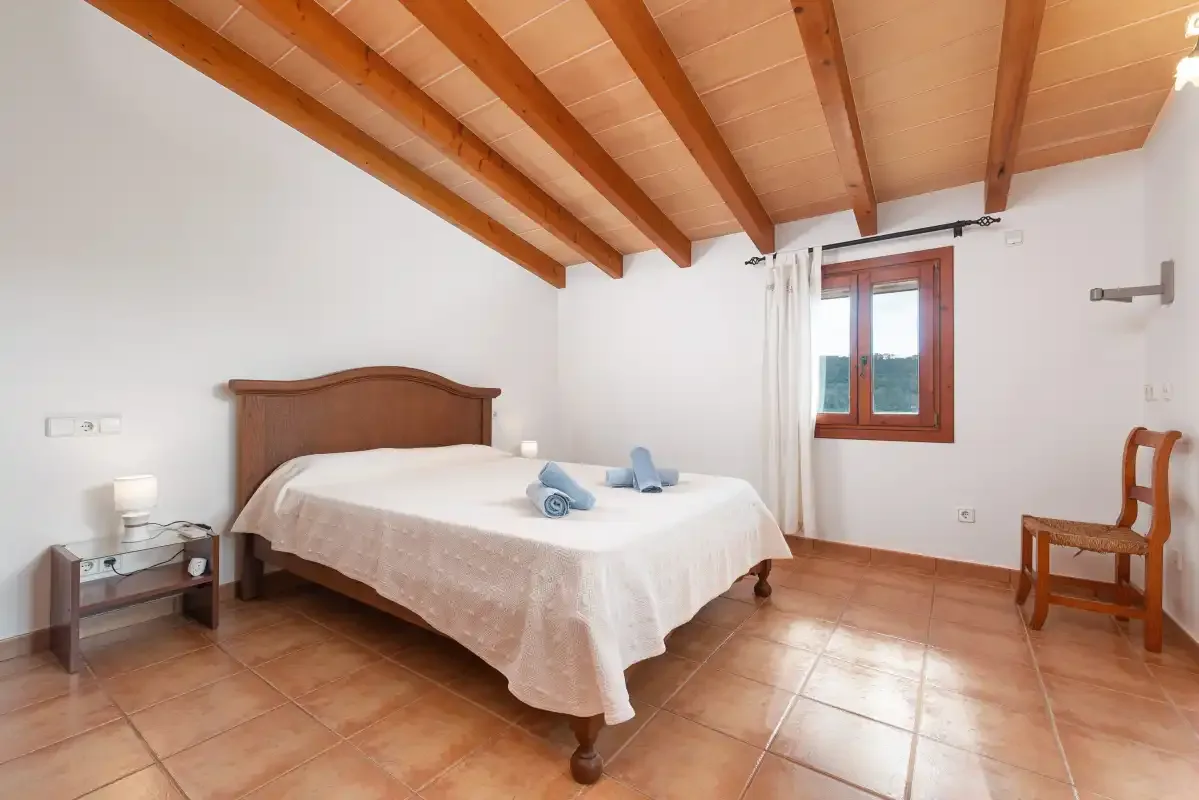 A bedroom with a double bed, wooden ceiling beams, and a window.
