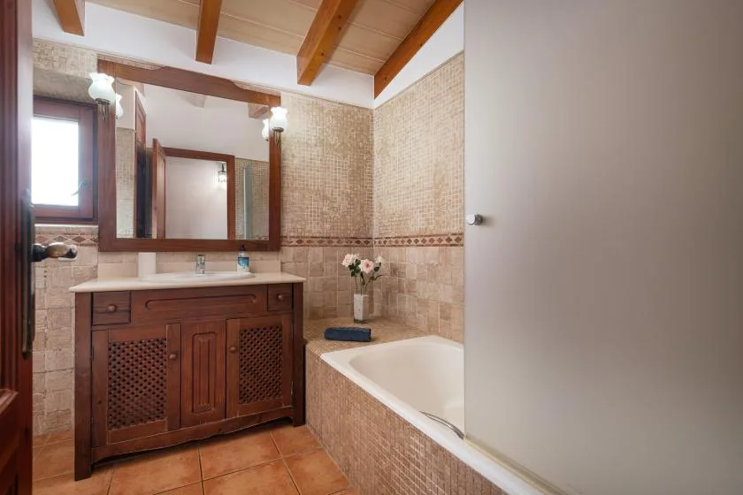 A tiled bathroom features a wooden vanity, mirror, and bathtub.