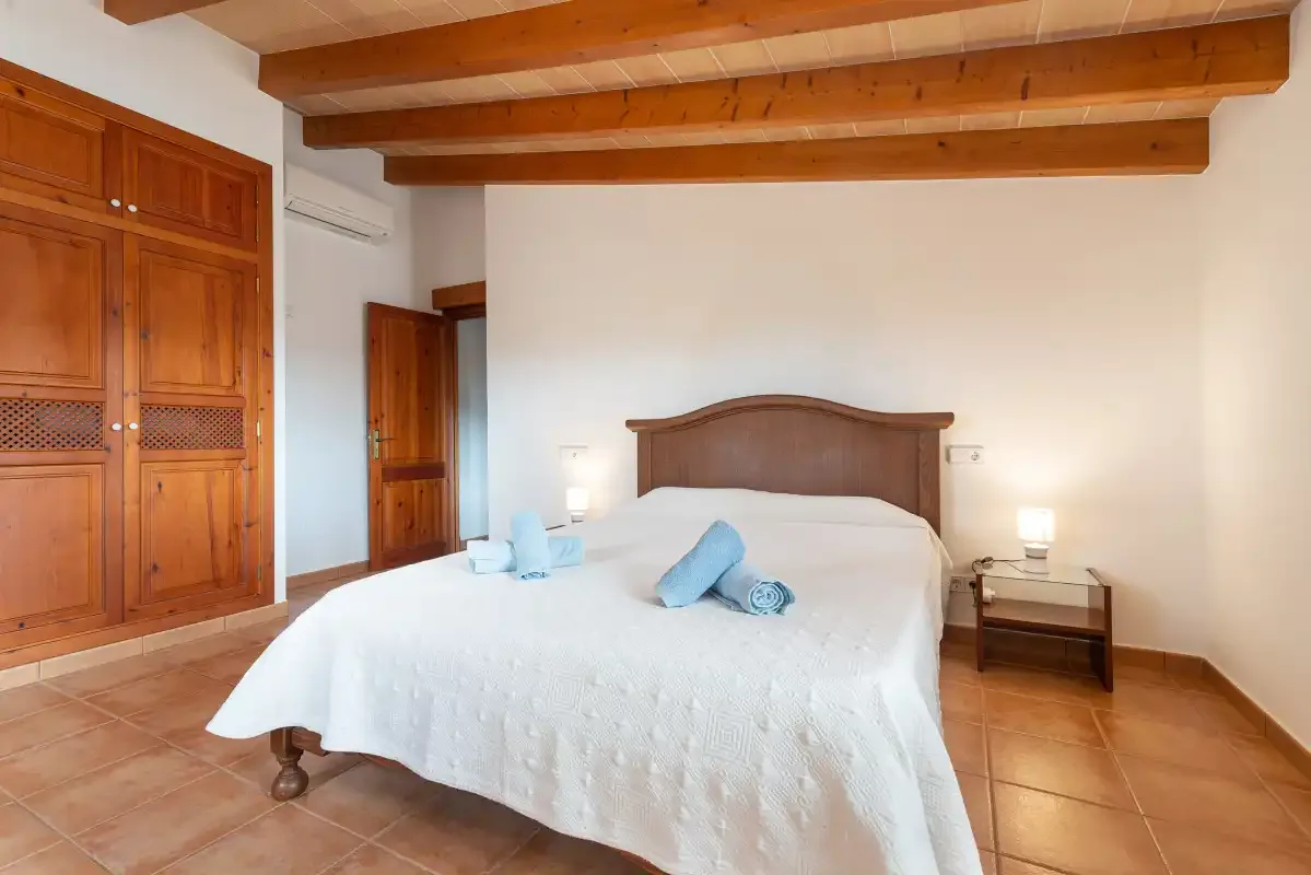 A bedroom with a bed, wooden wardrobe, and exposed ceiling beams.