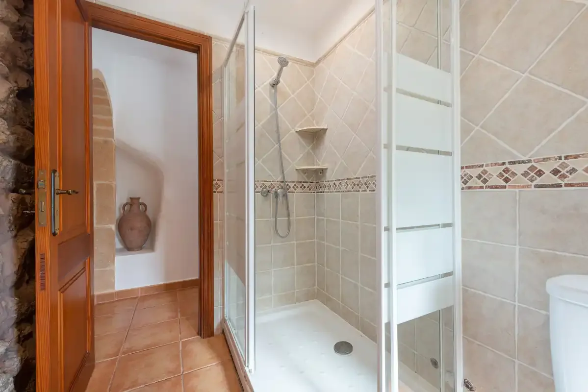 A tiled bathroom with a glass shower and a wooden doorway.
