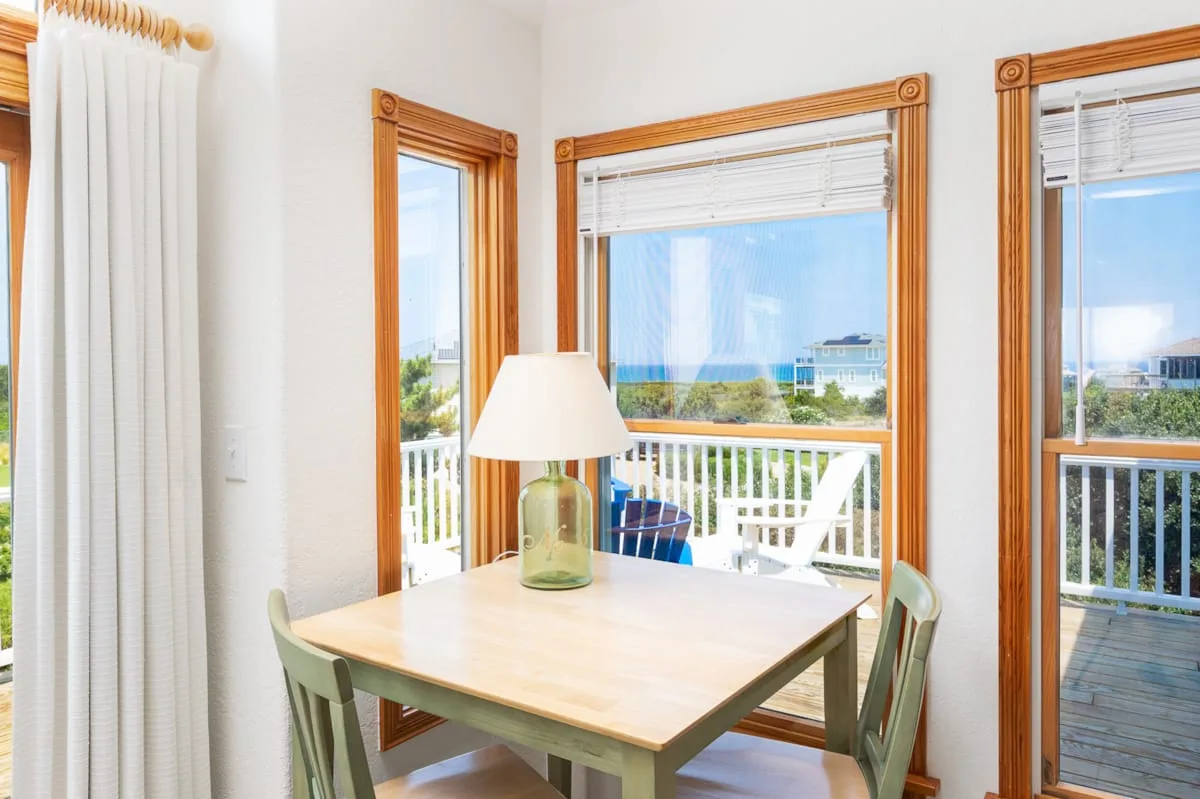 Un comedor luminoso con una mesa de madera junto a grandes ventanas que dan a un balcón.
