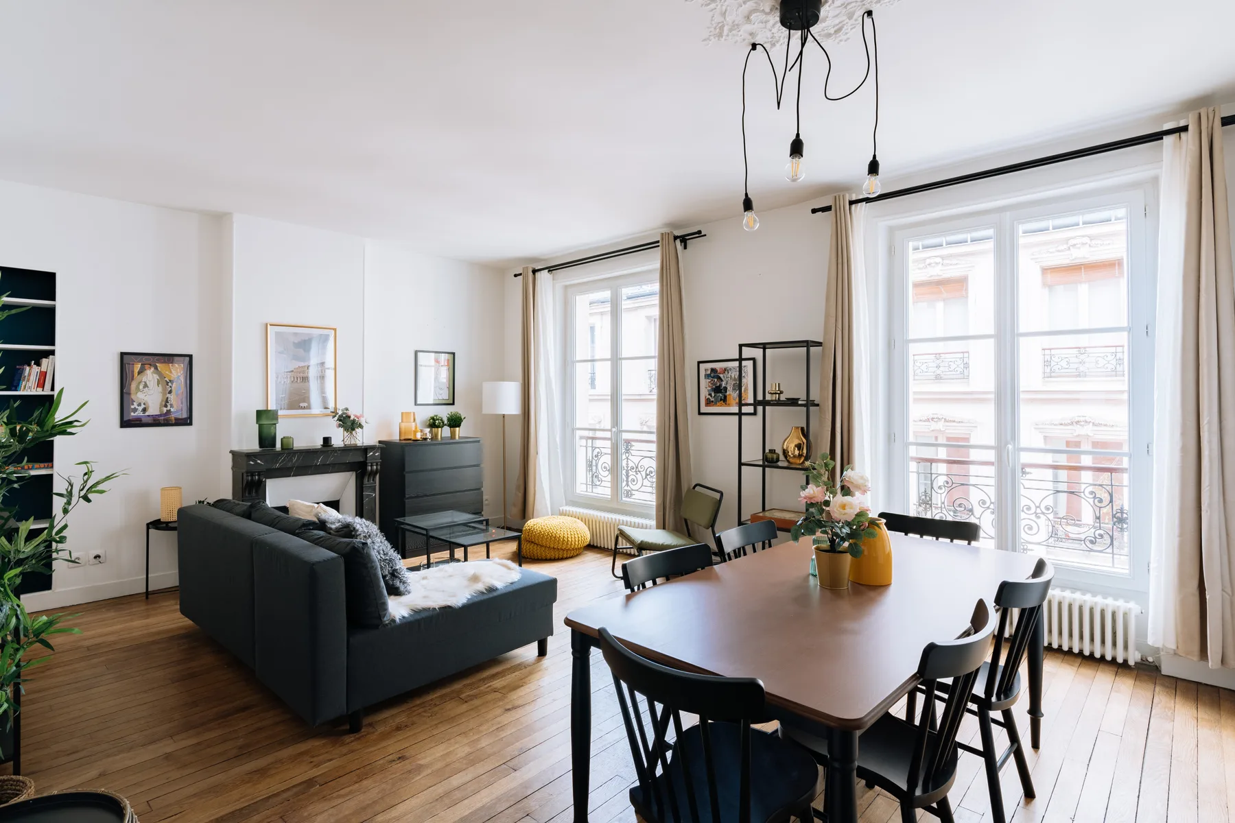 Una luminosa sala de estar y comedor con un sofá oscuro y una mesa alargada.