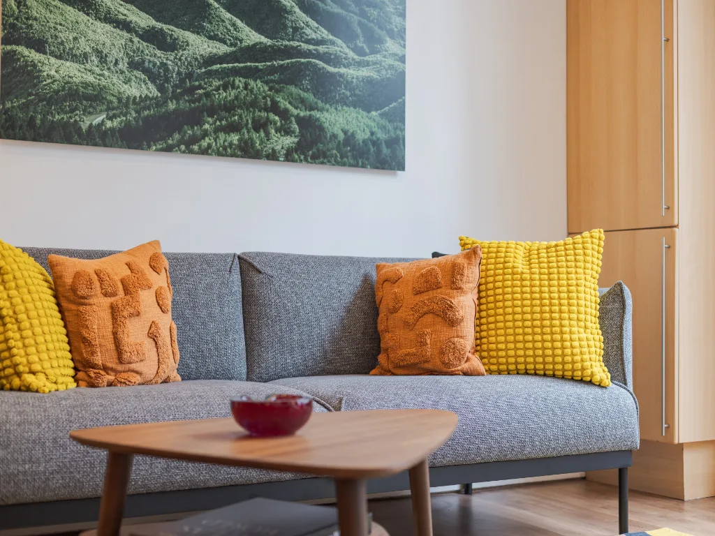 Una sala de estar con asientos grises, cojines coloridos y una mesa de centro de madera.