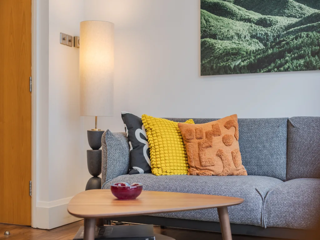 Zona de estar con un sofá gris, cojines y una mesa de centro.
