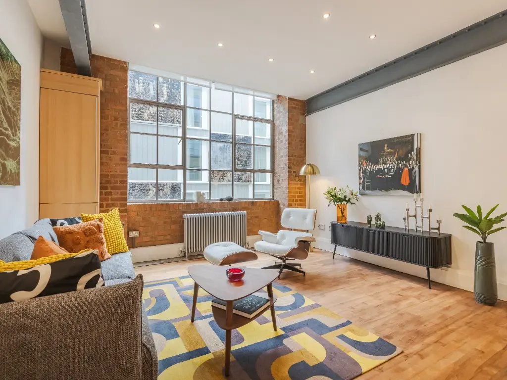 Una sala luminosa con asientos, una mesa de centro y grandes ventanas de estilo industrial.