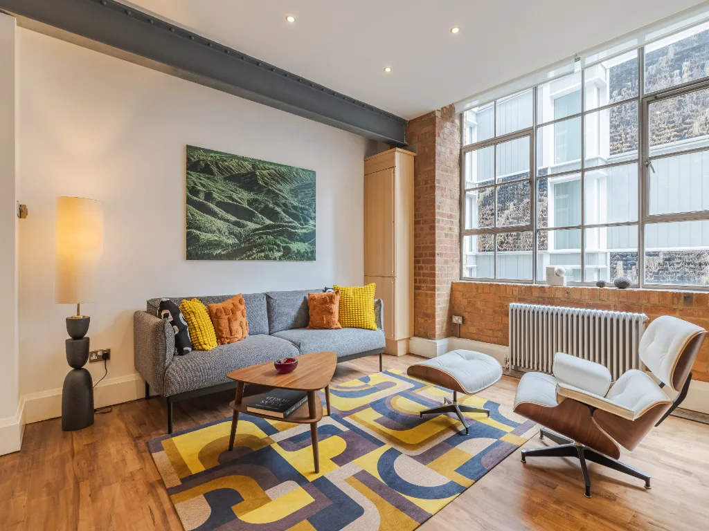 Una sala luminosa con asientos alrededor de una alfombra colorida y una mesa de centro.