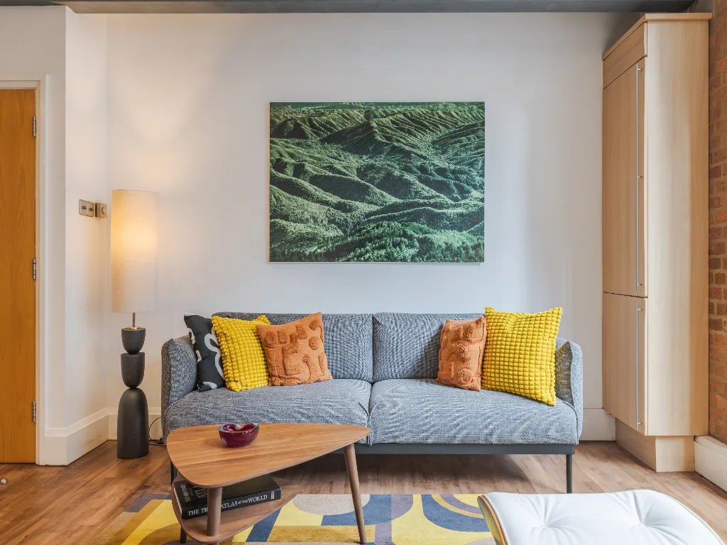 A living room with a gray seating area, colorful cushions, and a framed landscape picture.